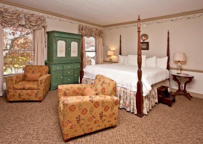 Four post bed in room with wallpaper, green armoire and two chairs